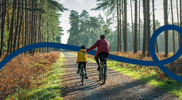 A father and son ride bikes through a forest representing good parenting.